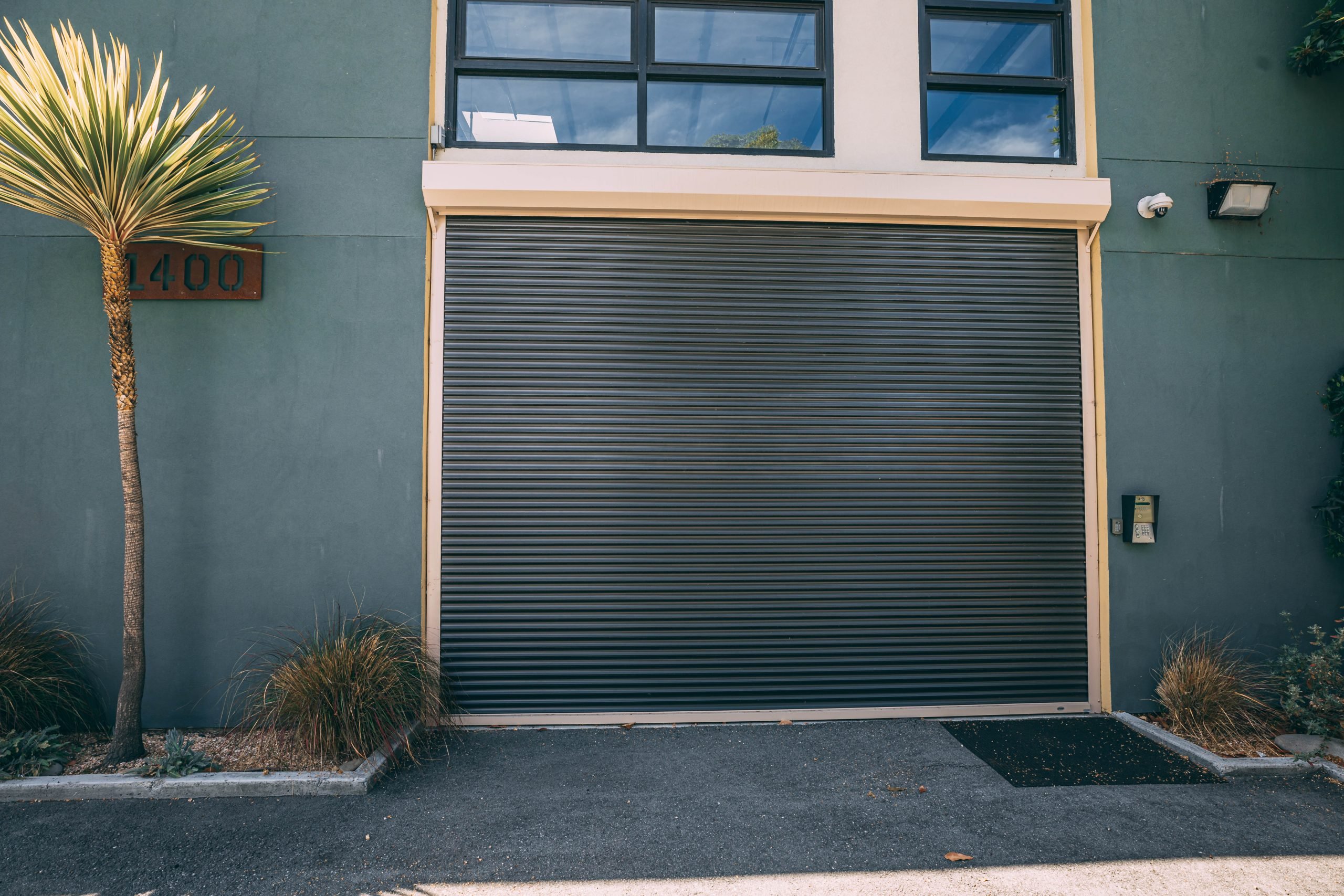 Overhead rolling commercial door installed on building wall next to palm tree